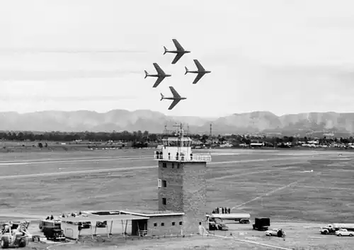 Four single-engined swept-wing jets in a diamond formation above an air base