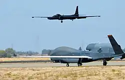 An RQ-4 Global Hawk taxies on the flight-line as a U-2 Dragon Lady makes its final approach at Beale Air Force Base during 2013.