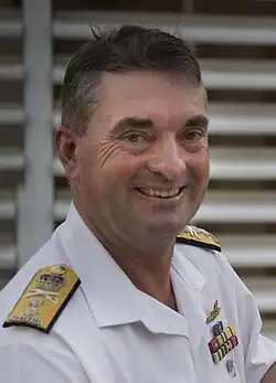 Colour photo of a man wearing a white uniform standing behind a lectern