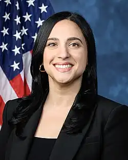 Official House portrait of Ansari smiling in front of the U.S. flag, wearing a black shirt.