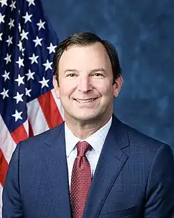Official House portrait of Goldman smiling in front of the U.S. flag, wearing a black jacket, light blue shirt, and checkered red tie.