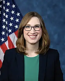Official House portrait of McBride smiling in front of the U.S. flag, wearing a black blazer jacket and green shirt.