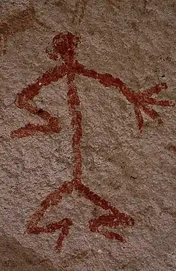 Humanoid stick figure painted on a rock wall in red. The figure is shown in Stylistic group C.