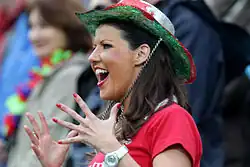 A women in Wales-flag cowboy hat, a red rugby shirt and with red painted fingernails smiles and cheers from the stand during the 2011 Rugby World Cup match between Wales and Fiji.