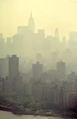 A morning skyline of New York City, with docks and the ocean visible at the bottom and progressively thicker haze into the distance. Only the outlines of far buildings can be seen, with details like windows or architectural features impossible to distinguish.