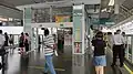 A photograph of Sengkang station's LRT platform. It is composed of a single platform with a white set of glass-claded columns in the middle. Both sides of the platform feature fixed barriers. The platform is crowded with people