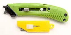 A modern safety cutter at top, with blunted tip blade and cutting guide/tape hook. At bottom, an older style simple plastic box cutter using standard straight edged blades.