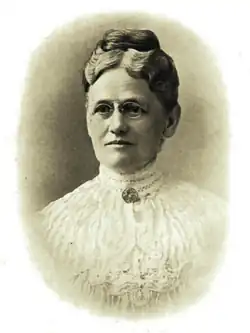 B&W portrait photo of a woman with her hair in an upd=-do, wearing a white blouse with a brooch at the neckline.