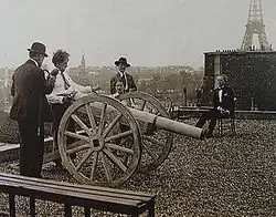 four people in suits stand on a Parisian rooftop; the Eiffel Tower is visible in the background