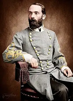 Colorized photo of a bearded man seated in a chair. He wears a gray military uniform with two rows of gold buttons and yellow frogging on the sleeves.
