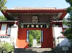 Small wooden gate painted in red, green and blue. Boards with Chinese characters are attached to the gate.