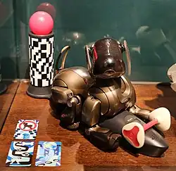 A Champagne Brown ERS-7 charging, positioned next to an AIBOne and AIBO cards.