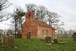 A small, simple brick church seen from the southwest in a churchyard, with a single bellcote at the west end