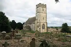 A stone church seen from the northwest. The tower is battlemented, and the relatively small plain body of the church extends beyond it