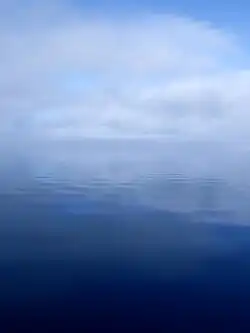 A calm, flat river surface with clouds and fog obscuring the horizon line