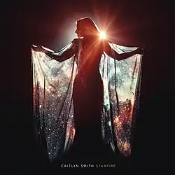 The cover features a woman covered in shadows with a bright light behind her, wearing a cape dress that shows the galaxy. Both the artist's name and album title appear below her, colored in white and orange respectively.