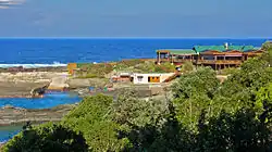 A large wooden building on a rocky promontory with sea and surf in the background