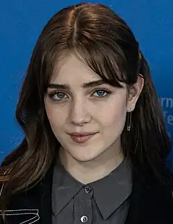 Talia Ryder in a grey top and black jacket, smiling