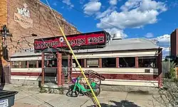 A single-story building in the shape of a railroad car, with an Art Deco facade in cream and maroon stripes situated next to a taller brick building