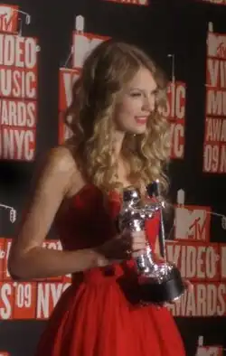 Side profile of Swift dressed in red, holding a trophy