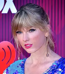 A color headshot of singer Taylor Swift posing for a photograph in front of a step and repeat.