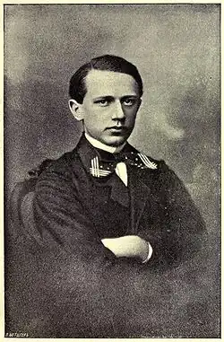 A clean-shaven man in his teens wearing a dress shirt, tie and dark uniform jacket.