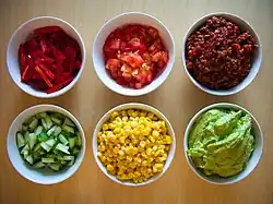 Small bowls containing corn, tomatoes, peppers, guacamole, and other ingredients