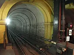 A narrow railway tunnel with a single railway track, lit by a bright white light