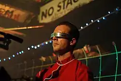 Professor Greg wearing a red uniform and wrap around visor.