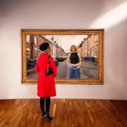 A photo of a woman inside a museum room looking at a large painting of another woman stood in the middle of a city street.