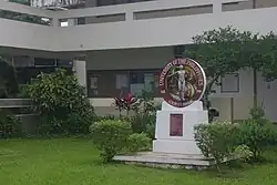 Tacloban College, Tacloban, Philippines. There is a green lawn in front of a white building, with a sign reading "UNIVERSITY OF THE PHILIPPINES 1908 - 2008 CENTENNIAL" in front.