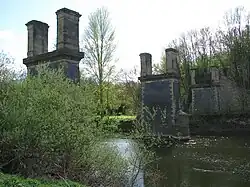 The remains of a victorian bridge spanning a large river. The bridge is incomplete and does not connect the two sides, only having pillars made of stone and brick.