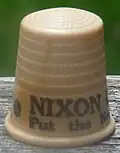 An off-white thimble, with the visible black lettering, "NIXON/Put the ne ...