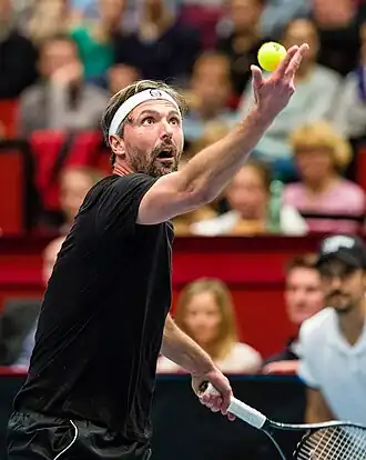Croatian tennis player Goran Ivanišević, shown from about the waist up, throwing a tennis ball in the air with a racquet in the other hand.