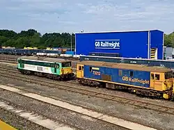Two diesel locomotives, behind which is a large blue building with "GB Railfreight" on the side