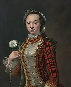 A young woman in a coat of predominantly-red tartan and white satin with gold braid, and a white headdress, with a white rose and what is probably a riding crop