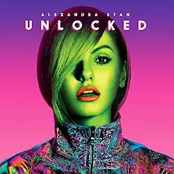 Stan shown sporting a multicolored jacket in front of a pink–purple background.