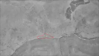 An aerial view of a deep stream valley with a road running left to right and smaller valleys joining it from top and bottom. A red roughly triangular shape is in the center.