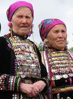 Two older women wearing national costume, featuring bright pink headscarves and coin-covered dresses.