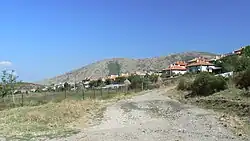 A dirt road looking towards a group of houses with mountains in the background