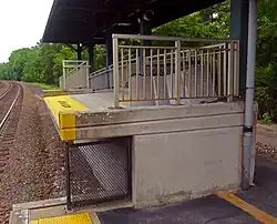 A small elevated platform with metal guardrails under a roof next to a curving railroad track
