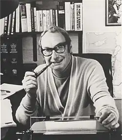 The author and former CIA operative Wilbur Crane Eveland sitting at a desk in front of a typewriter brandishing a pipe