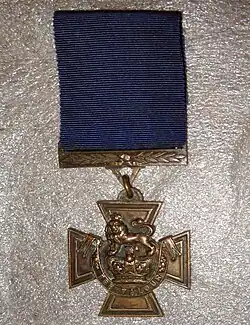 The obverse of the bronze cross pattée medal; showing the crown of Saint Edward surmounted by a lion with the inscription FOR VALOUR with a blue ribbon