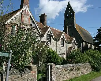 A row of cottages, partially obscured by vegetation. In the background is the bell tower of a much larger building.