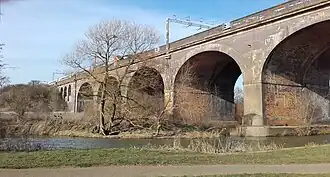 Five of the six arches of a tall bridge across a broad shallow river.