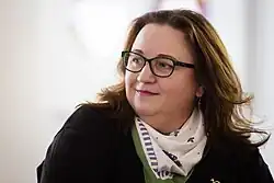 portrait of a woman with brown hair and dark spectacles, facing left, very light background