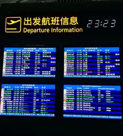 Four monitors with information on the departures of flights displayed in different colors of text on backgrounds of varying shades of blue. Three are in Chinese and one is in English. At the top is an icon with an airliner taking off and, in yellow, the words "Departure Information" in English and Chinese next to it. In the upper right is the time, 23:23, in white digital letters
