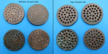 Four corroded metal dies are shown on the left, and their other sides on the right. The bottom side has small holes and the top sides have larger ones. Each die has 40 to 50 matching holes in it. Each die is slightly different, to produce different sizes of spaghetti or similar pasta noodles.